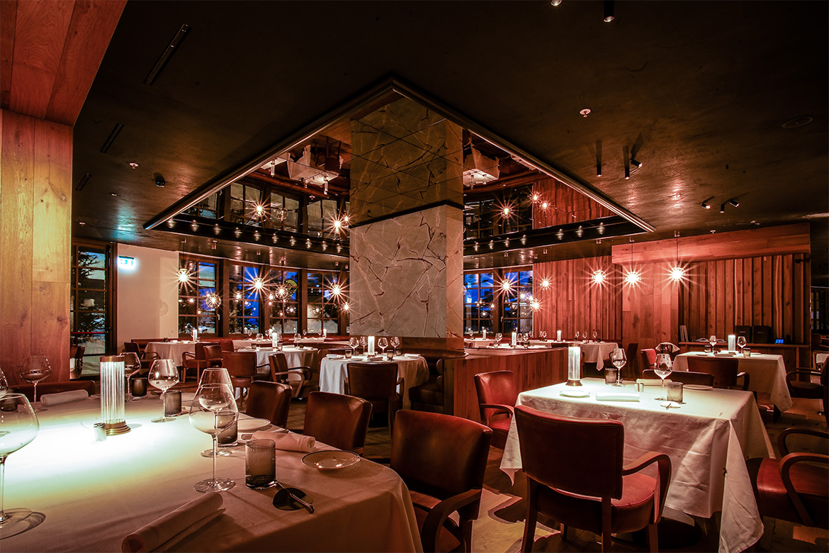 Ristorante elegante in Hotel Al Piolet con tavoli apparecchiati, sedie imbottite, pareti in legno, illuminazione calda e atmosfera raffinata da montagna.