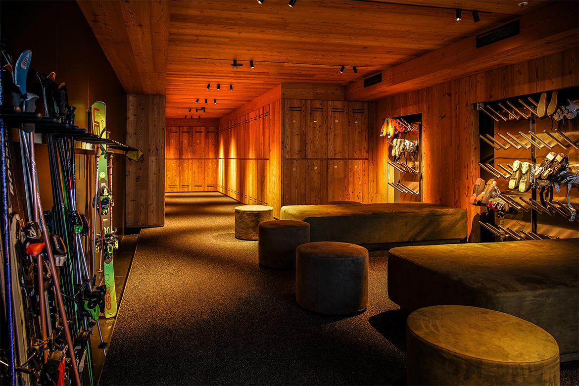 Ski room in Hotel Al Piolet con armadietti in legno, deposito sci e snowboard, sedute imbottite e illuminazione calda in stile alpino.