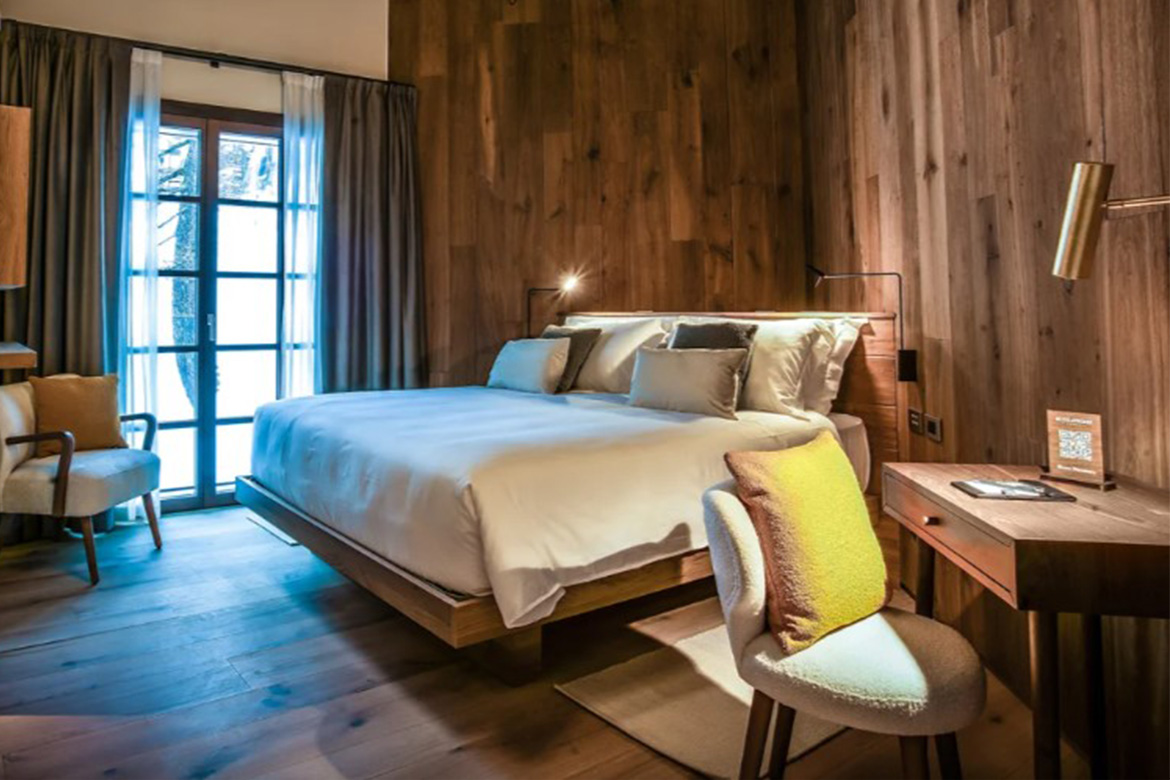 Camera matrimoniale accogliente in Hotel Al Piolet con pareti e pavimento in legno, letto sospeso, scrittoio, poltroncine e atmosfera calda da montagna.