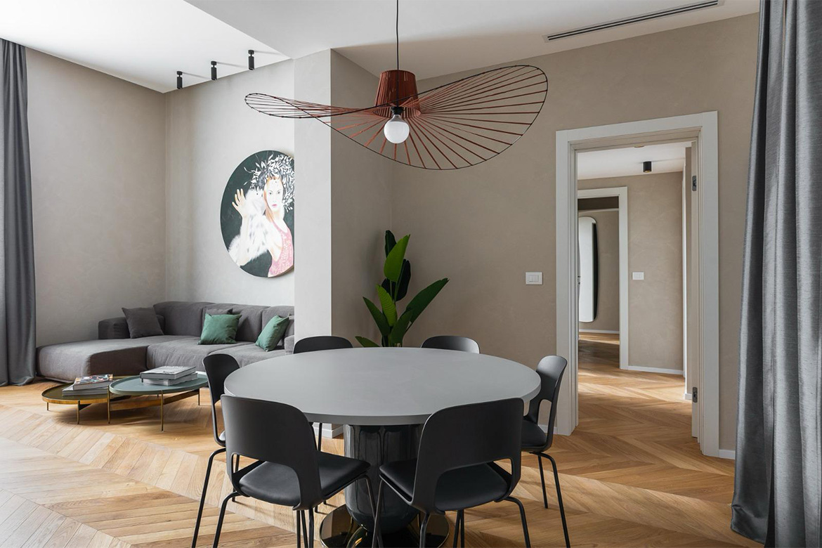 Zona giorno moderna con tavolo rotondo, sedie nere, divano, tavolini, lampada a sospensione decorativa e arredi Pianca Contract per B&B San Martino.