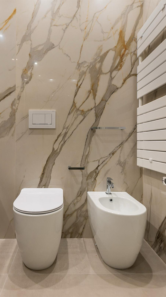 Bagno moderno con sanitari bianchi, rivestimento effetto marmo, termoarredo bianco e dettagli contemporanei per B&B San Martino.