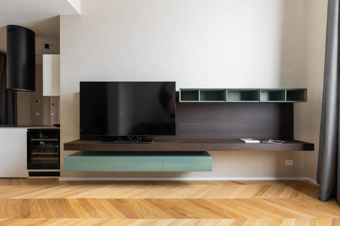 Zona living moderna con mobile TV sospeso, finiture in legno scuro e verde chiaro, pavimento in legno e arredi Pianca Contract per B&B San Martino.