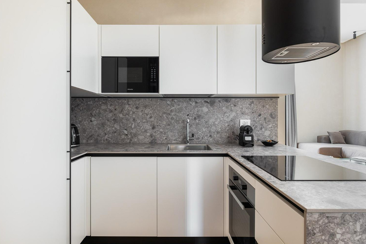 Cucina moderna con mobili bianchi, piano in pietra grigia, piano a induzione, cappa nera e arredi Pianca Contract per B&B San Martino.