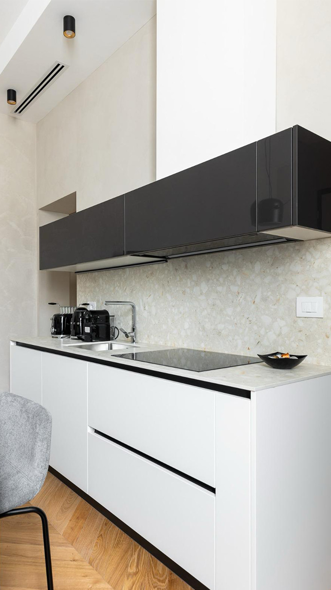 Cucina moderna compatta con basi bianche, pensili neri lucidi, piano a induzione, lavabo integrato e arredi Pianca Contract per B&B San Martino.