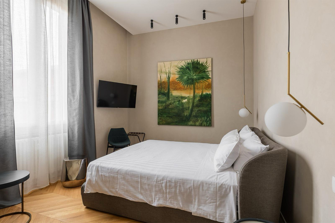 Camera B&B elegante con letto imbottito, lampade sospese, pavimento in legno e arredi Pianca Contract.