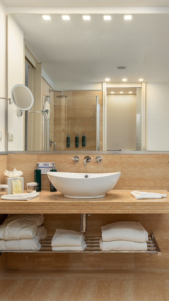 Bagno moderno in DoubleTree Hilton con lavabo da appoggio, grande specchio, piano effetto marmo, doccia in vetro e arredi Pianca Contract.