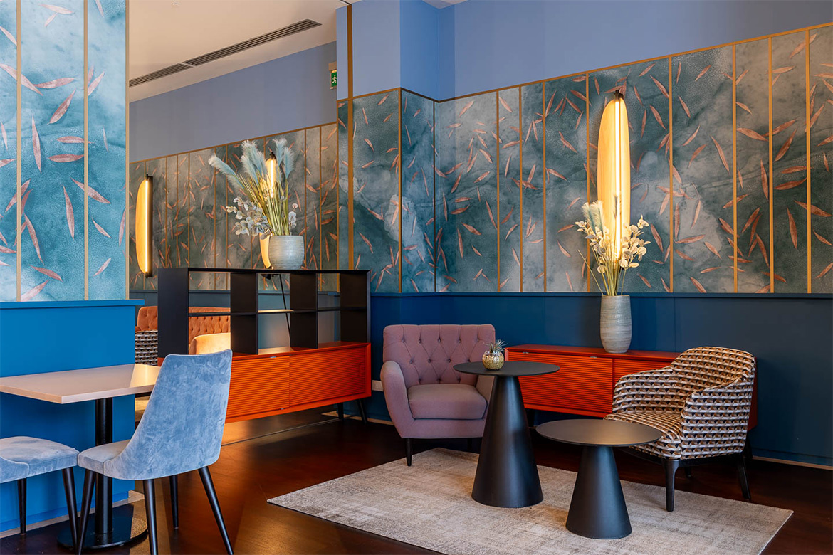 Area lounge moderna in DoubleTree Hilton a Firenze con poltrone colorate, tavolini neri, pareti decorative azzurre, madie arancioni e arredi Pianca Contract.