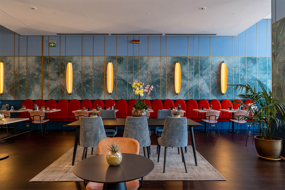 Sala ristorante moderna in DoubleTree Hilton a Firenze con sedute rosse, tavoli eleganti, pareti decorative azzurre, applique luminose e arredi Pianca Contract.