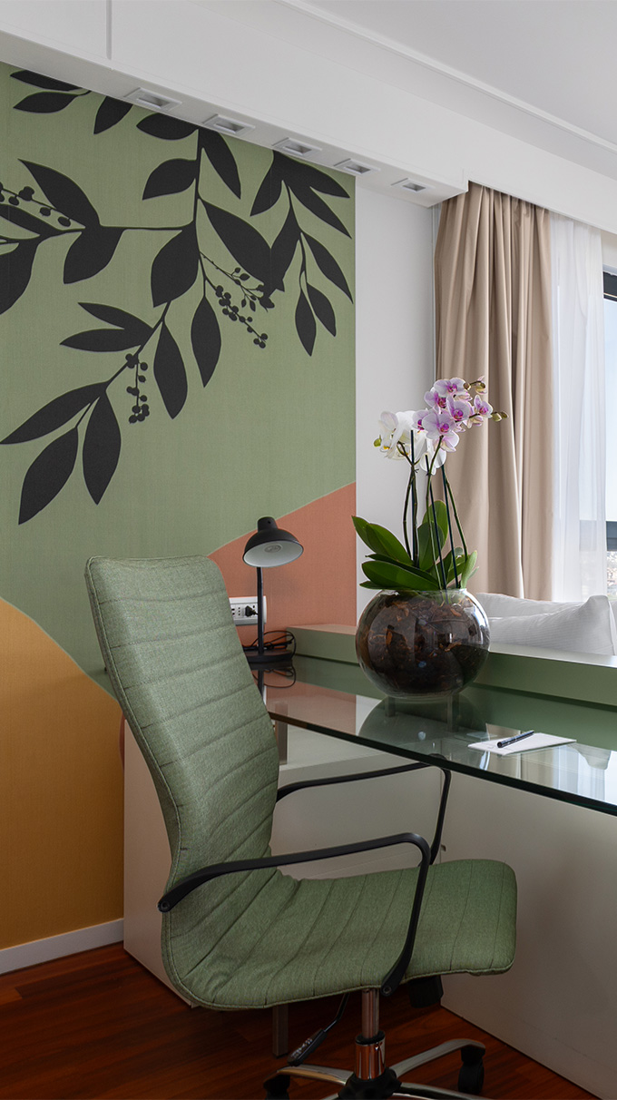 Angolo studio moderno in DoubleTree Hilton a Firenze con scrivania in vetro, sedia imbottita verde, parete decorativa botanica, orchidea e arredi Pianca Contract.