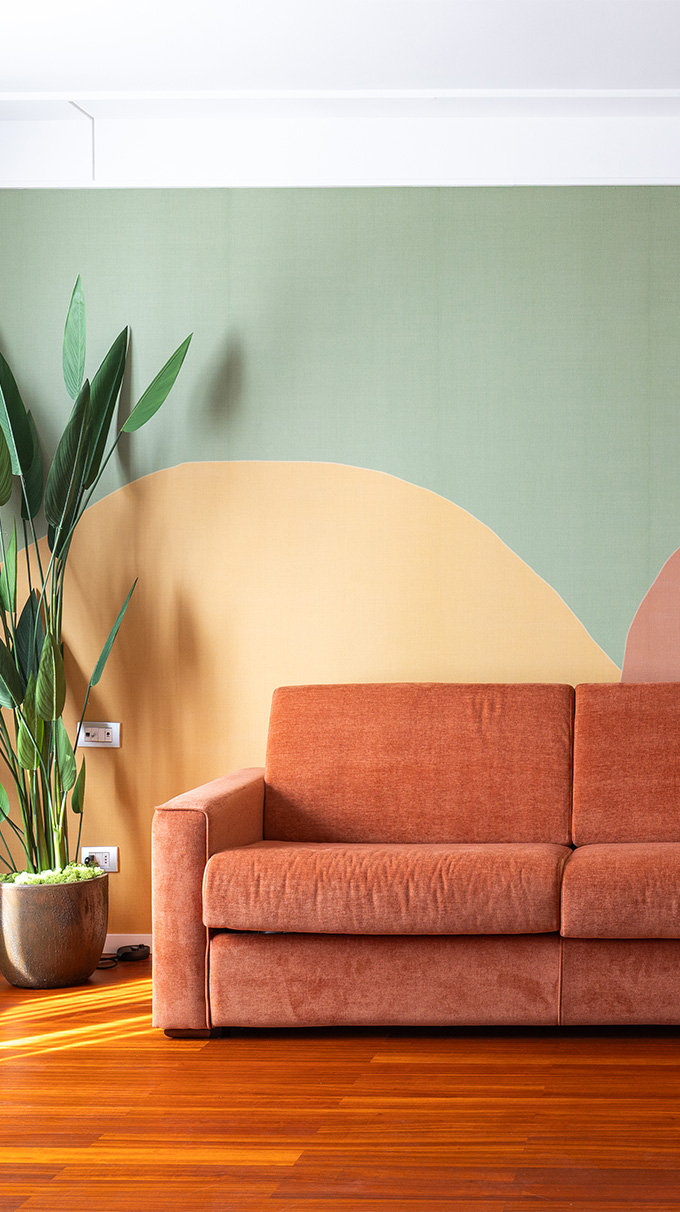 Zona living moderna in DoubleTree Hilton a Firenze con divano arancione, parete decorativa verde, pianta ornamentale, pavimento in legno e arredi Pianca Contract.