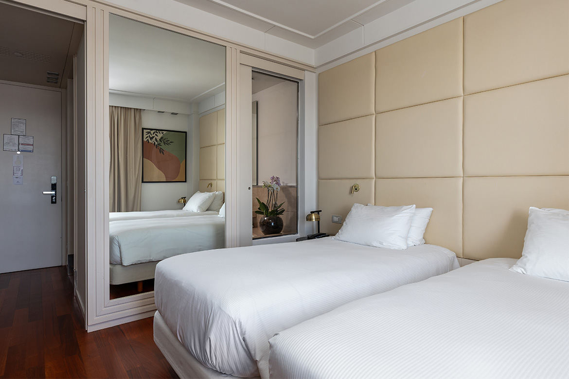 Camera doppia elegante in DoubleTree Hilton con due letti singoli, testiera imbottita beige, armadio con ante a specchio, pavimento in legno e arredi Pianca Contract.
