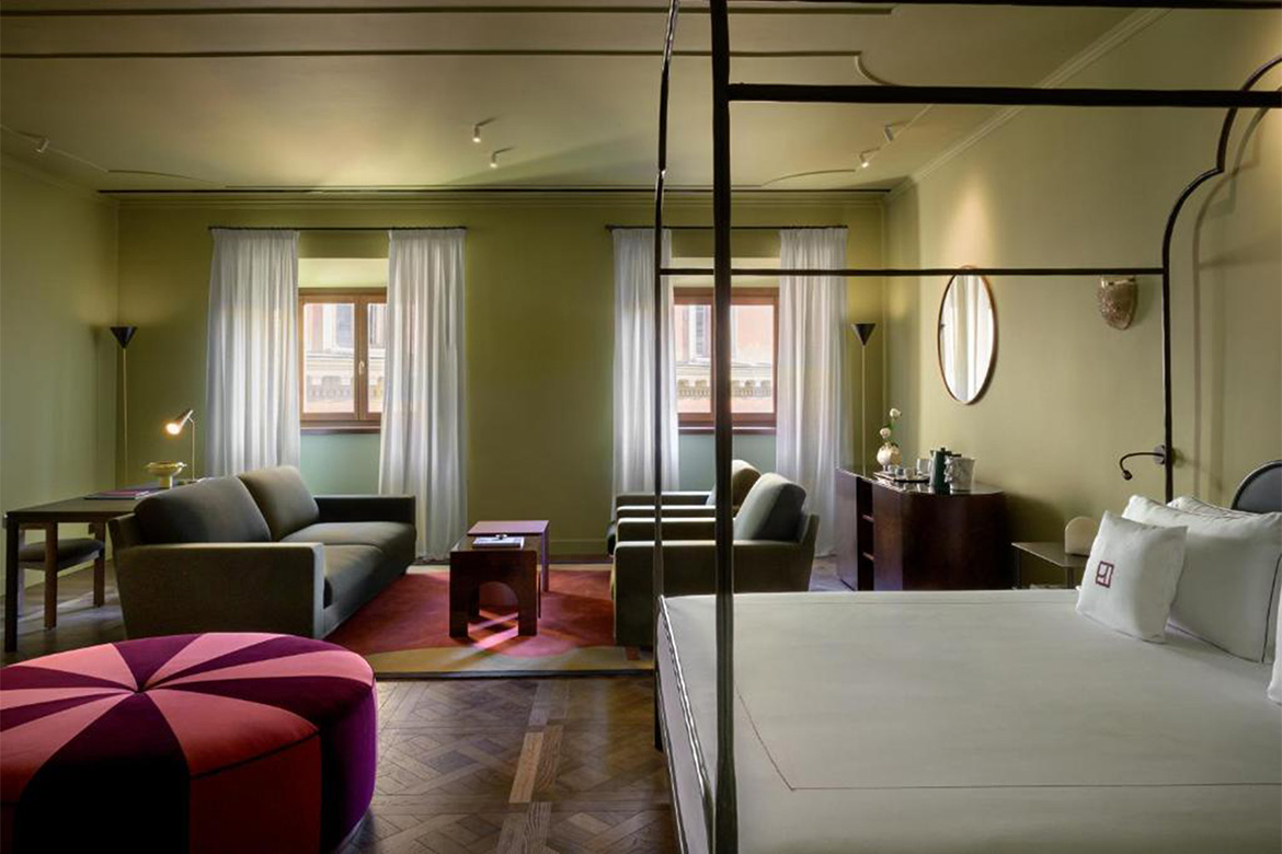 Suite elegante in Hotel Talia a Roma con letto a baldacchino, zona living, divano, scrittoio, pouf colorato, pavimento in legno e arredi Pianca Contract.