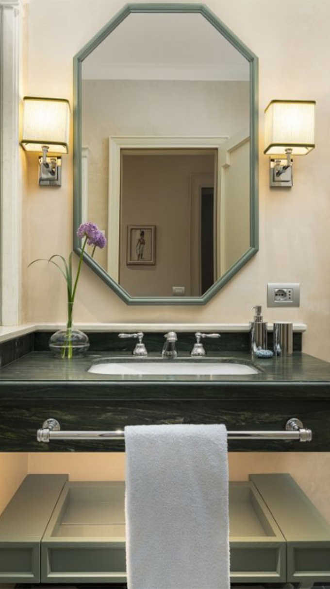 Bagno elegante in hotel veneziano con lavabo in marmo verde, specchio ottagonale, applique laterali e dettagli raffinati Pianca Contract.
