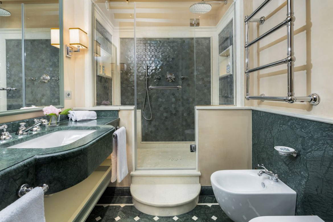 Bagno elegante in hotel veneziano con lavabo in marmo verde, doccia in vetro, bidet, termoarredo cromato e dettagli raffinati Pianca Contract.